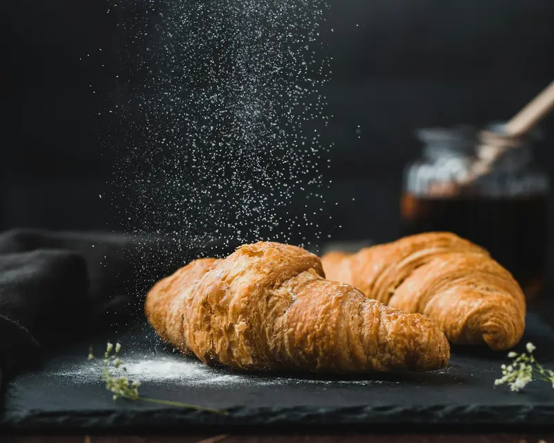 A golden croissant being dusted with sugar