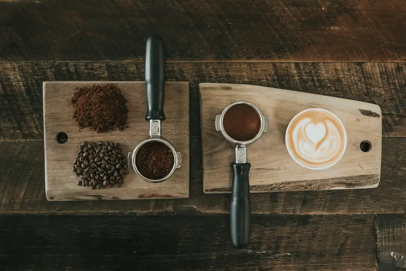 Ground coffee, a portafilter and a latte laid out on a wooden board