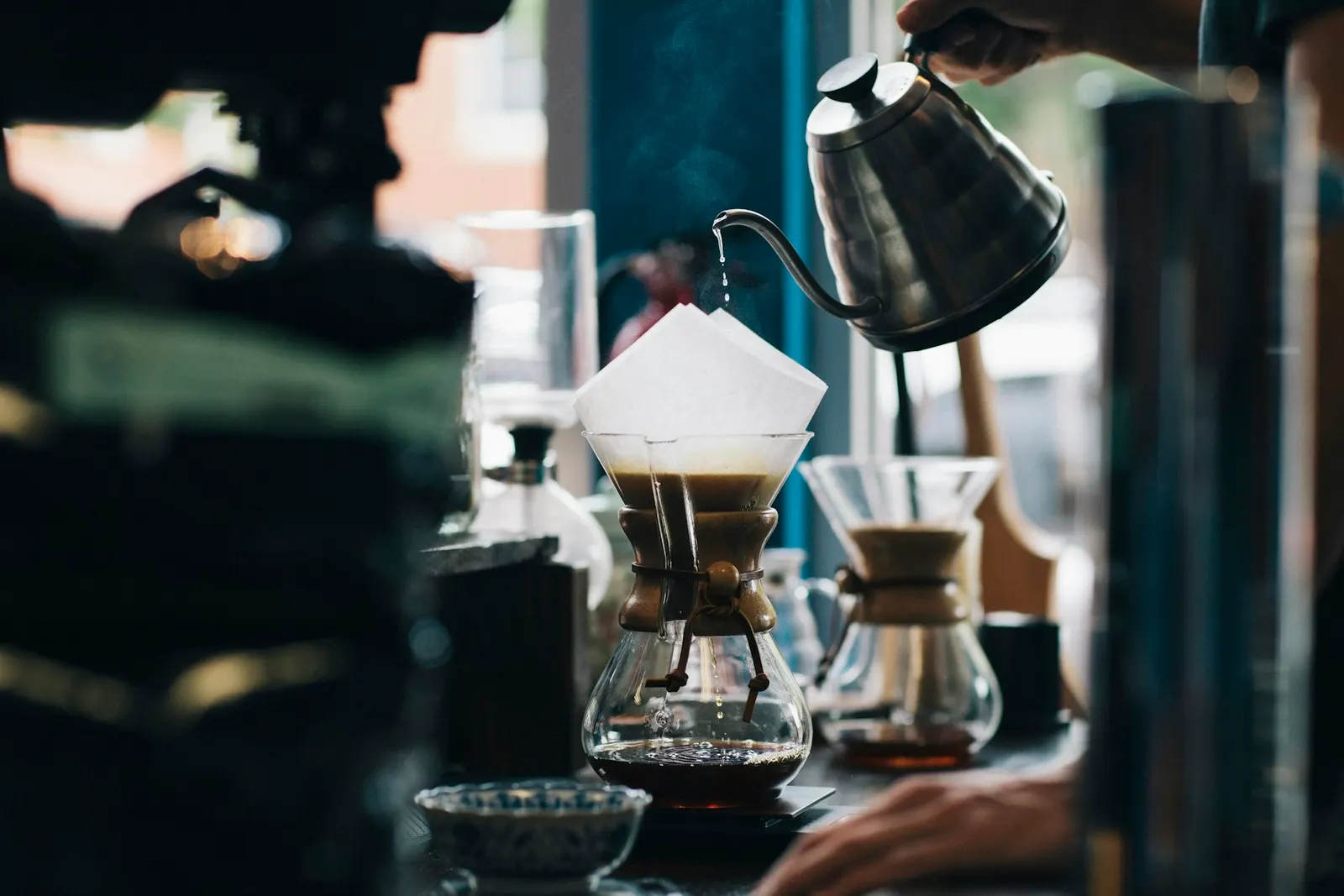 A barista pouring water over a glass dripper at the bar